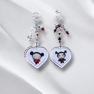 K&ouml;nnte beinhalten: Zwei herzf&ouml;rmige Schl&uuml;sselanh&auml;nger mit Pucca und Garu aus der Zeichentrickserie Pucca. Jeder Schl&uuml;sselanh&auml;nger hat einen silbernen Anh&auml;nger mit roten, schwarzen und wei&szlig;en Perlen.