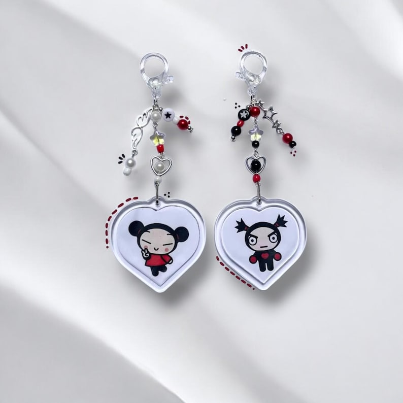 K&ouml;nnte beinhalten: Zwei herzf&ouml;rmige Schl&uuml;sselanh&auml;nger mit Pucca und Garu aus der Zeichentrickserie Pucca. Jeder Schl&uuml;sselanh&auml;nger hat einen silbernen Anh&auml;nger mit roten, schwarzen und wei&szlig;en Perlen.