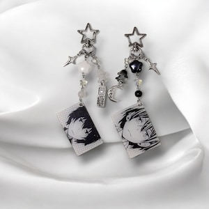 Peut inclure: Deux boucles d'oreilles à breloques argentées avec des breloques de personnages d'anime en noir et blanc, des perles blanches et des étoiles, des lunes et d'autres breloques argentées.