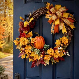 K&ouml;nnte beinhalten: Ein runder Herbstkranz aus braunen Zweigen, verziert mit einem zentralen orangefarbenen K&uuml;rbis, gelben und roten Seidenbl&auml;ttern, orangefarbenen Blumen und kleinen Beeren. Eine gro&szlig;e, mehrlagige Schleife aus gold-orange-gr&uuml;nem Karoband sitzt oben.