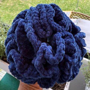 Könnte beinhalten: Ein großer Ball dunkelblauer Wolle, aus weichen, flauschigen Fasern. Die Wolle ist fest gewickelt und scheint bereit zum Stricken oder Häkeln zu sein.