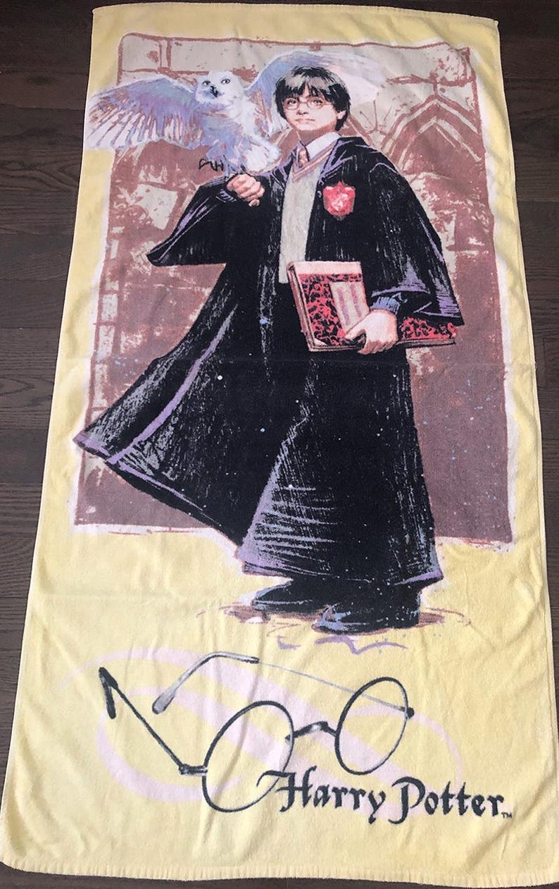 May include: A yellow beach towel with a cartoon image of Harry Potter holding a book and an owl. The towel has the text "Harry Potter" printed on it.