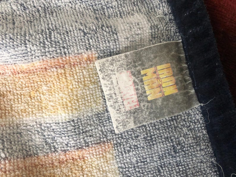 May include: A striped towel with a blue border and a white label that says "MARVEL" in black letters.