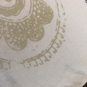 May include: Close-up of a cream-colored fabric with a large, beige floral design. The design is a stylized paisley pattern. The fabric has a ribbed texture.