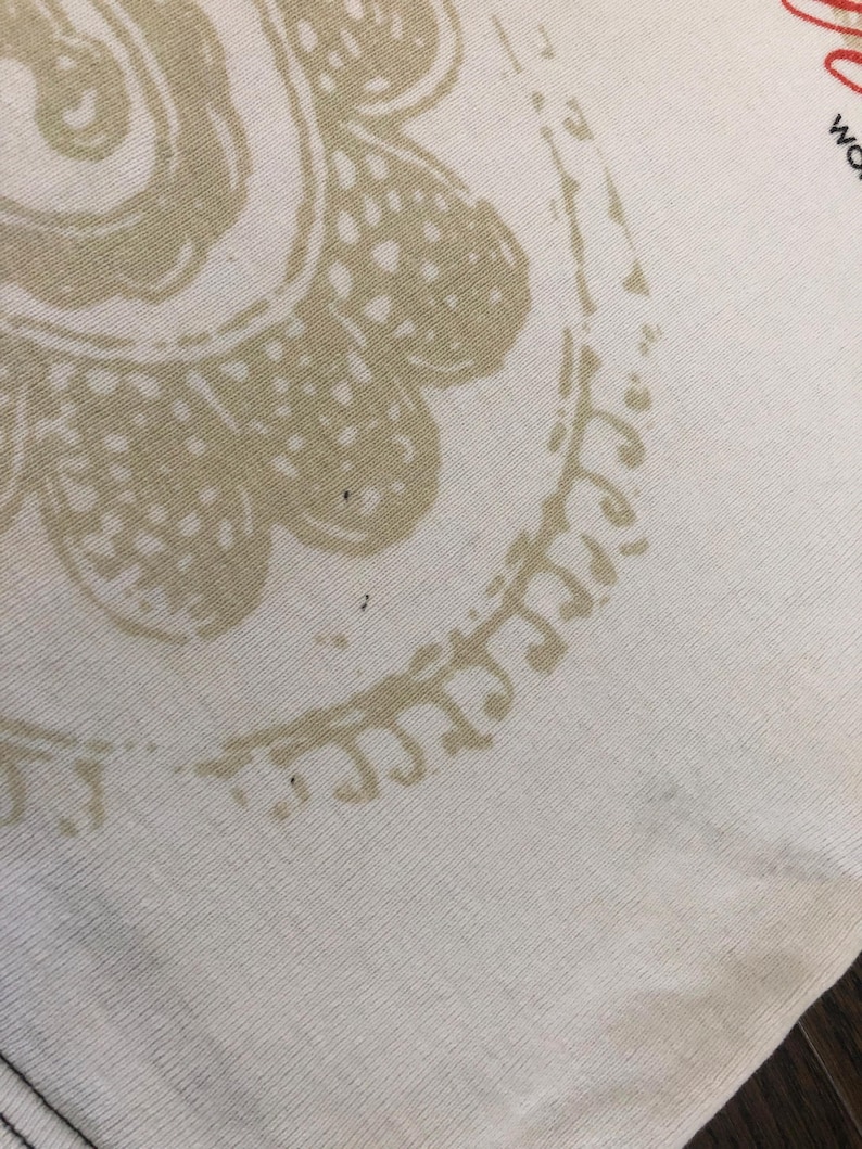 May include: Close-up of a cream-colored fabric with a large, beige floral design. The design is a stylized paisley pattern. The fabric has a ribbed texture.