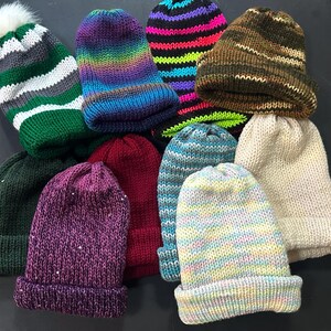 Könnte beinhalten: Sortiment von zehn gestrickten Mützen in verschiedenen Farben und Mustern, darunter grün, weiß, lila, blau, rot, braun, beige und rosa.