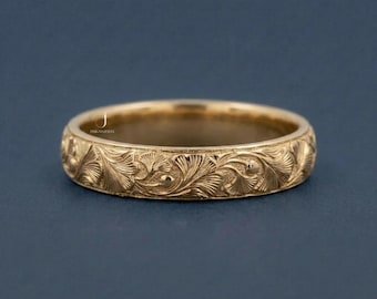 May include: A gold ring featuring an elaborate floral design. The ring's surface is covered in detailed carvings of leaves and swirling patterns. The ring is set against a dark blue background, accentuating its ornate details.