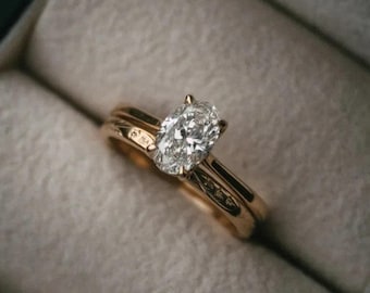 Può includere: Un anello di fidanzamento in oro con un diamante taglio ovale, presentato in un cofanetto di velluto grigio. L'anello è un simbolo di impegno e amore, ideale per un'occasione speciale.