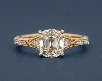 May include: A gold ring featuring a central cushion-cut stone held by four prongs. The band displays intricate filigree metalwork and is accented with small round diamonds embedded along the sides of the shank, showcasing a detailed design.