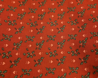 May include: Close-up of a red fabric with a repeating pattern of green holly leaves, red berries, and small white hearts. The fabric has a slightly textured appearance, suggesting a woven material. The design is festive and suitable for holiday-themed projects.