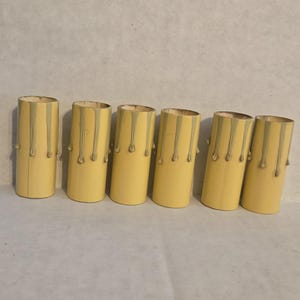 May include: Six cylindrical candle sleeves in a row. The sleeves are a pale yellow with a dripping wax design in a darker yellow. The sleeves are for a chandelier or candelabra.