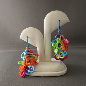 Puede incluir: Un par de pendientes colgantes de colores con forma de Mickey Mouse. Los pendientes est&aacute;n hechos de pl&aacute;stico y est&aacute;n suspendidos de ganchos plateados.