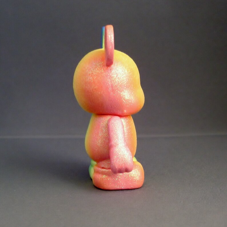 May include: A pink and yellow glittery toy with a blue and yellow horn. The toy is shaped like a bear and has a rounded body.