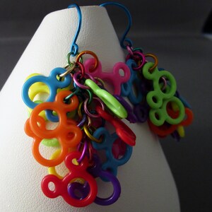 Puede incluir: Pendientes colgantes coloridos con m&uacute;ltiples dijes de pl&aacute;stico con forma de orejas de Mickey Mouse. Los dijes est&aacute;n unidos por una cadena plateada y cuelgan de ganchos plateados.