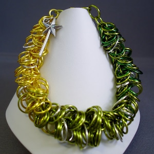 以下が含まれることがあります： 銀色の星形のチャームが付いた、緑と金のチェーンメイルブレスレット。ブレスレットは、小さな金属製の輪が互いにつながって作られています。