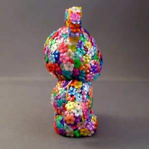 Op de afbeelding: Een kleurrijk speelgoedfiguurtje in de vorm van een konijn, bedekt met kleine plastic bloemen in verschillende kleuren, waaronder roze, blauw, groen, geel en paars.