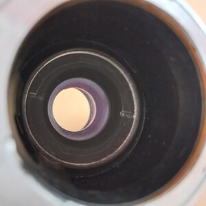 Op de afbeelding: Een close-up van binnen in een cilindrisch object, met concentrische cirkels. De binnenkant is voornamelijk zwart, met een lichtbruine cirkel in het midden. Een dunne, paars getinte ring omringt de centrale cirkel.