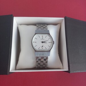 May include: A vintage silver-toned wristwatch with a white face, black hands, and the word "ПОБЕДА" printed on the dial. The watch is in a black and white box, resting on a white pillow. The watch band is also silver-toned.