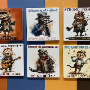 May include: Set of six square ceramic coasters featuring colorful illustrations of cats playing musical instruments. Each coaster has an inspirational quote. The quotes are: "Throw me to the wolves, and I will come back LEADING THE PACK!" "Just because my path is different, DOESN'T MEAN I'M LOST!" "STRONG PEOPLE Lift others up!" "Start each day with a GRATEFUL HEART" "Ask yourself what makes you come alive and GO DO IT!" "FIND WHAT MAKES YOU happy and GET LOST IN IT"