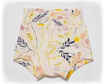 May include: Cream-colored baby shorts with a floral pattern. The design features yellow, pink, and navy blue flowers and foliage. The shorts have a high waist and a comfortable fit, perfect for everyday wear.