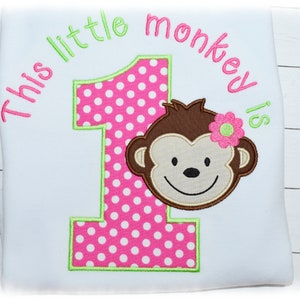 May include: White t-shirt with the text "This little monkey is". The number 1 is pink with white polka dots and a green outline. A brown monkey face with a pink flower is on the right.