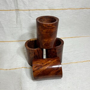 Puede incluir: Cuatro tazas de madera apiladas una encima de la otra. Las tazas son de madera oscura con un tono marrón rojizo y un patrón de veta de madera natural.
