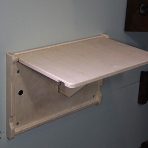 May include: A light wood folding table mounted to a wall. The table is made of plywood and has a simple design.