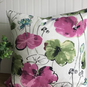 May include: Square decorative pillow with a floral pattern. The pillow features large, watercolor-style flowers in shades of pink, green, and blue against a white background. The design includes leaves and stems, creating a botanical theme.