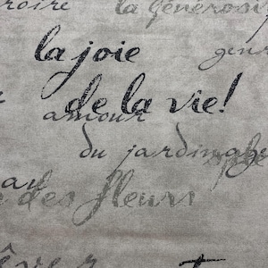 May include: A close-up of a beige fabric with black text printed on it. The text reads "la joie de la vie!" and "du jardinage des fleurs".
