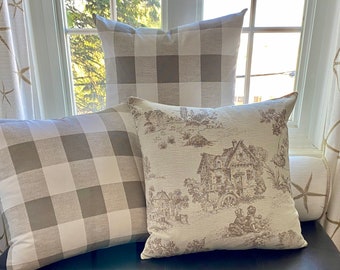 May include: Three decorative throw pillows, two with a white and gray gingham pattern and one with a beige background and a brown toile pattern of a house and trees.