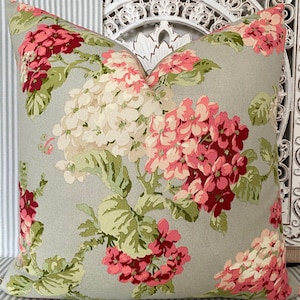 May include: A grey pillow with a floral pattern featuring pink, white and green flowers. The pillow is made of a soft, textured fabric.