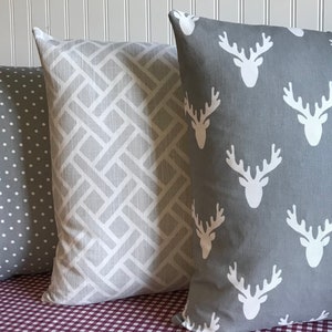 May include: Three decorative throw pillows with different patterns. The first pillow is grey with white polka dots. The second pillow is grey with a white geometric pattern. The third pillow is grey with a white deer silhouette pattern.