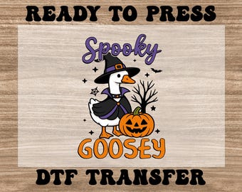 May include: A Halloween-themed graphic featuring a goose in a witch hat and cape, holding a jack-o'-lantern. The words "Spooky Goosey" are displayed in orange and purple text, with the words "Ready to Press" and "DTF Transfer" above and below.