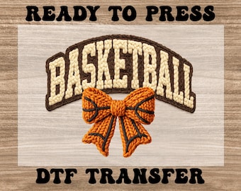 May include: A basketball-themed DTF transfer design. The design features the word "BASKETBALL" in a brown and cream-colored arched banner, with an orange and black basketball bow below. The words "READY TO PRESS" and "DTF TRANSFER" are above and below the design.