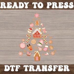 May include: A Christmas tree design composed of various gingerbread cookies and holiday-themed elements. The design includes gingerbread houses, candy canes, ornaments, and the text "READY TO PRESS" and "DTF TRANSFER". The image is set against a wood grain background.