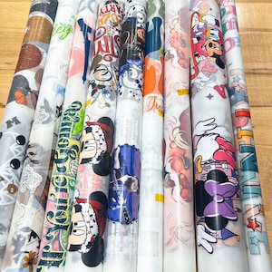 May include: A collection of rolled decorative papers with various designs. The designs include Mickey and Minnie Mouse, floral patterns, and text. The papers are in a variety of colors, including red, blue, green, and white. The papers are rolled up and ready for use.