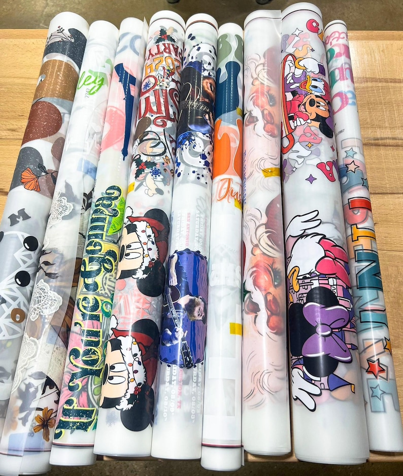 May include: A collection of rolled decorative papers with various designs. The designs include Mickey and Minnie Mouse, floral patterns, and text. The papers are in a variety of colors, including red, blue, green, and white. The papers are rolled up and ready for use.