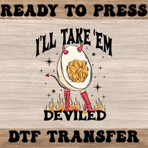 May include: A DTF transfer design featuring a deviled egg character with devil horns, a tail, and red boots, standing on flames. The text "I'll Take 'Em" and "Deviled" are above and below the egg.