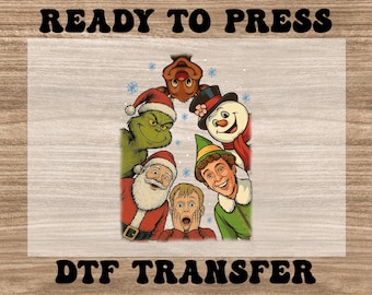 May include: DTF transfer featuring a festive design with holiday characters including the Grinch, Santa Claus, a snowman, an elf, and a surprised child. The words "READY TO PRESS" and "DTF TRANSFER" are printed in black.