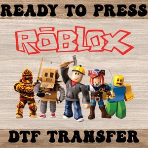 May include: A DTF transfer featuring the Roblox logo in red and several Roblox character figures. The characters include a knight, a robot, a builder, a pirate, and a yellow-headed figure. The words "READY TO PRESS" and "DTF TRANSFER" are above and below the image.