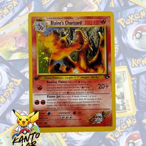 May include: A Blaine's Charizard trading card featuring a fire-type dragon illustration, 100 HP, and attacks Roaring Flames and Flame Jet. The card includes text detailing its evolution, abilities, and stats, with a 1st Edition stamp on the left side.