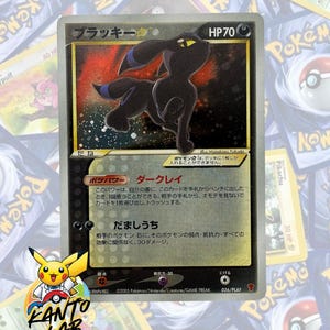 以下が含まれることがあります： 黒い体に青い輪の模様があるブラッキーのポケモンカード。HP70、背景は暗い星空のようなデザイン。カードには日本語のテキスト、名前「ブラッキー」、イラストレーター名「Masakazu Fukuda」が記載されている。