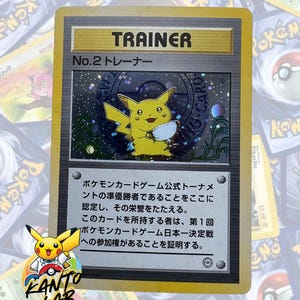 May include: A Trainer card featuring Pikachu from the Pokémon Trading Card Game. The card has a gold border and the text "TRAINER" at the top. The card also has Japanese text and a holographic image of Pikachu.