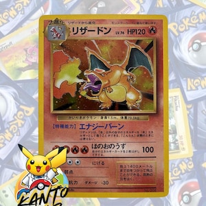 May include: A Charizard Pokémon card with a fiery orange and yellow design. The card features a detailed illustration of Charizard, a fire-breathing dragon, with Japanese text and the Kanto Lab logo.