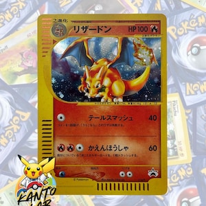 Puede incluir: Una carta coleccionable Pokémon japonesa de Charizard con una ilustración holográfica de la criatura naranja similar a un dragón con alas azules. La carta muestra 100 HP, símbolos de tipo fuego y texto en japonés, incluyendo el nombre Lizardon.