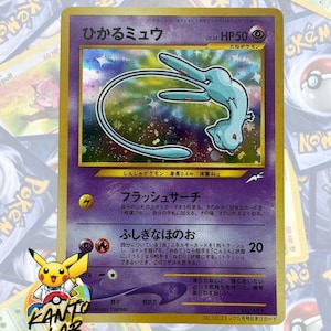 Puede incluir: Una carta coleccionable Pokémon "Shining Mew" japonesa con una ilustración holográfica de la criatura azul claro sobre un fondo morado. La carta muestra el texto "ひかるミュウ", "HP50" y "No. 151", junto con texto en japonés que detalla sus ataques "Flash Search" y "Mysterious Fire".