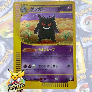 Puede incluir: Una carta coleccionable de Gengar con borde dorado, que muestra una criatura morada con ojos rojos y una amplia sonrisa. La carta presenta texto en japonés, la etiqueta HP 90 y una ilustración holográfica en un paisaje desértico.