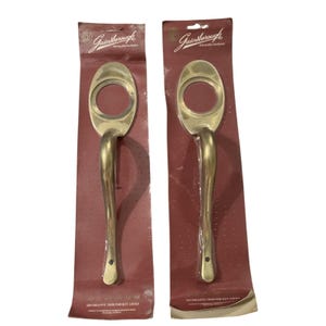 May include: Two brass-colored Gainsborough decorative door trim handles for key locks, packaged on maroon cards. Each handle has an oval top with a circular opening and a curved, elongated handle. The packaging includes the Gainsborough logo and text.