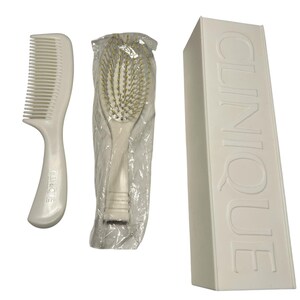 May include: A white hair care set featuring a comb, a brush in plastic packaging, and a rectangular box. The comb has a curved handle with the brand name. The brush has gold-colored bristles. The box has the brand name embossed on the side.