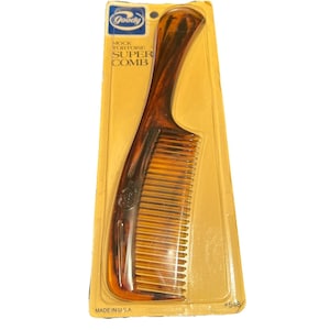 May include: A Goody Mock Tortoise Super Comb in its original packaging. The comb is a warm brown color with a tortoise shell pattern. The packaging is yellow and has the Goody logo at the top. The comb is made in the USA.